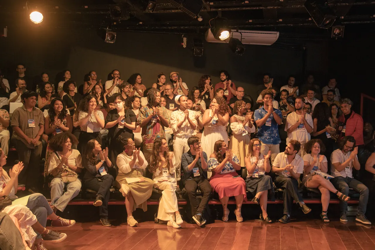Plateia aplaudindo, sentada no palco do teatro