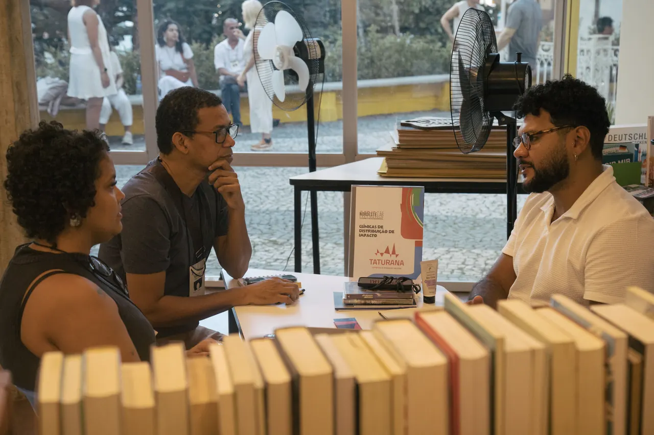 Três pessoas conversam em uma mesa com livros