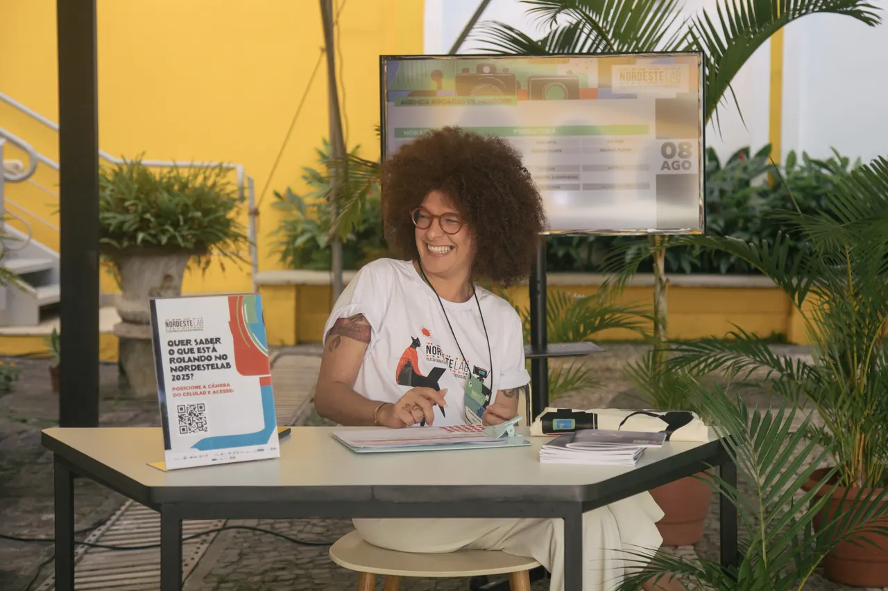 Participante sorri atrás de uma mesa de atendimento